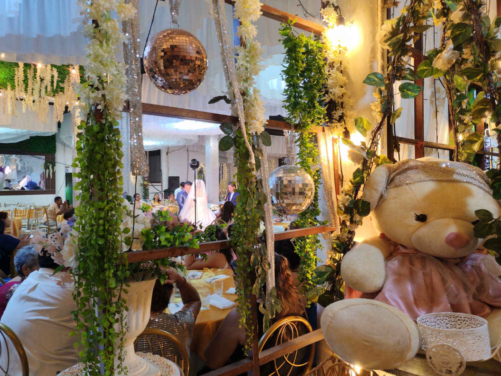 Ambientación con follaje natural, esferas espejadas y luces cálidas durante una boda